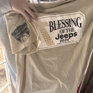 Taupe shirt with "Blessing of the Jeeps" on the front, and an OB-OJ logo on the sleeve of the shirt.