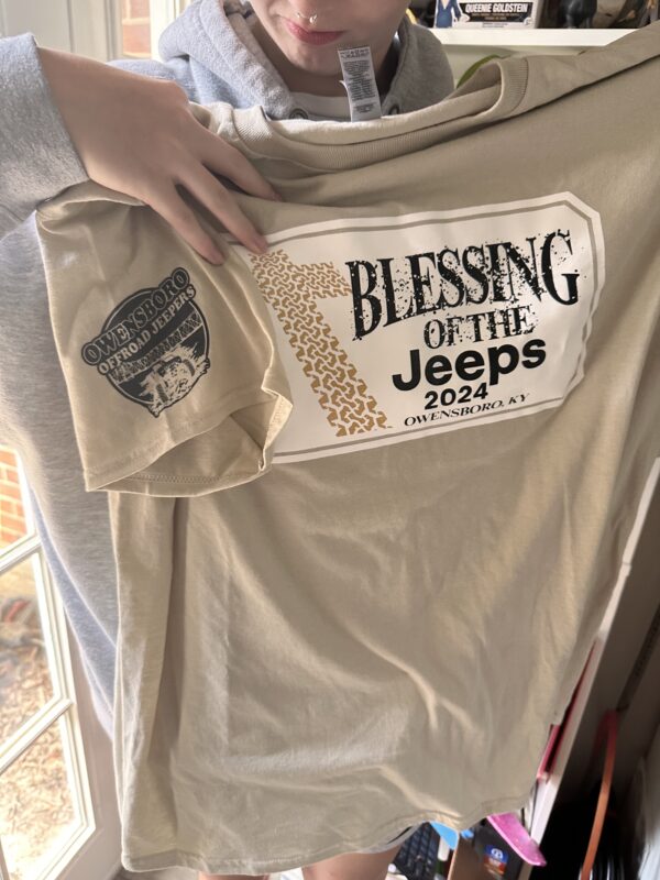 Taupe shirt with "Blessing of the Jeeps" on the front, and an OB-OJ logo on the sleeve of the shirt.